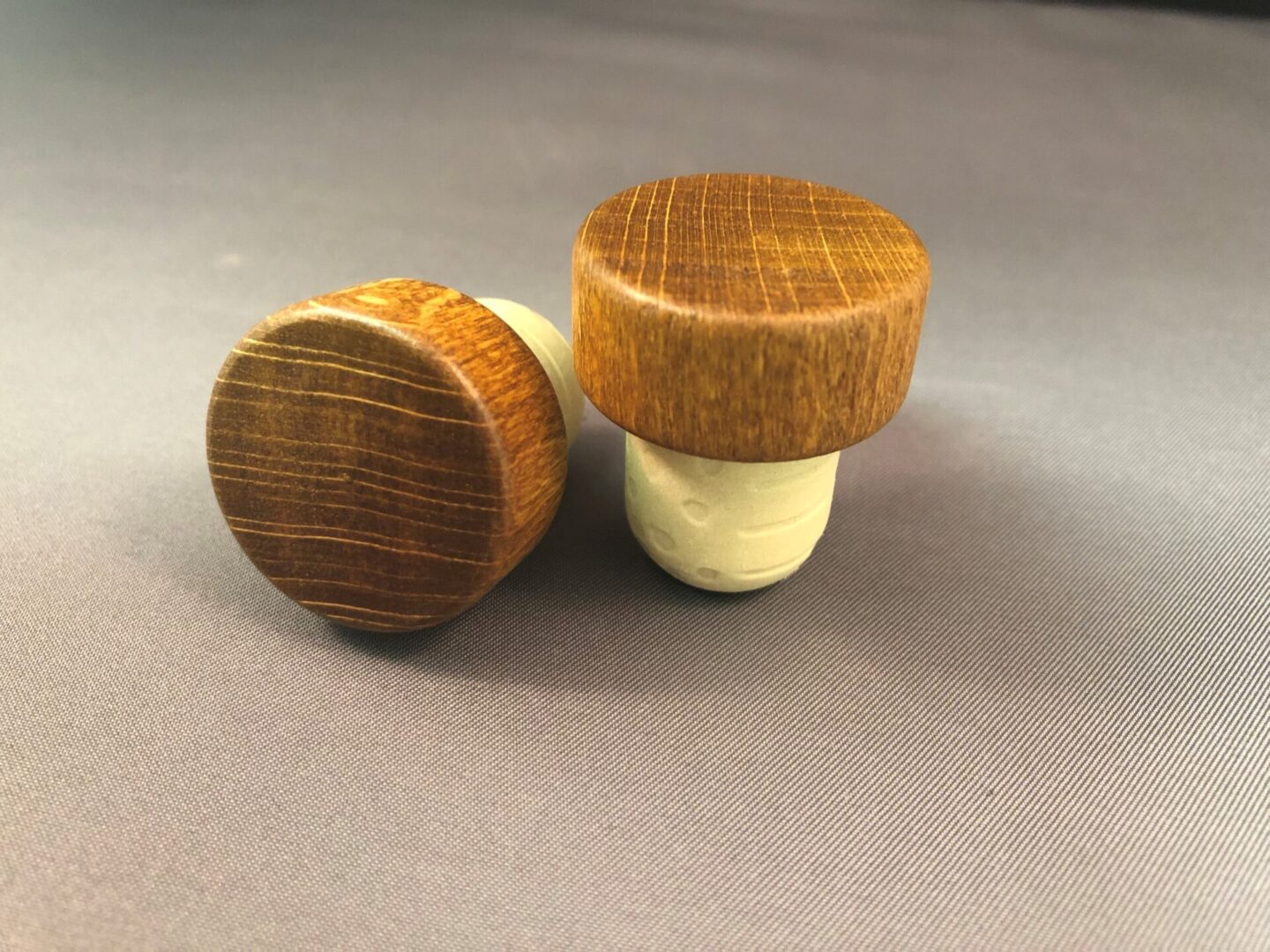 Two Café Brown 29x13/19.5 wooden wine stoppers on a grey surface.