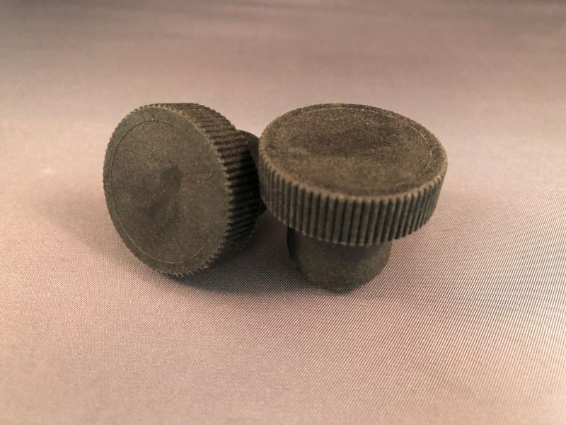 Two black plastic knobs on a grey surface.