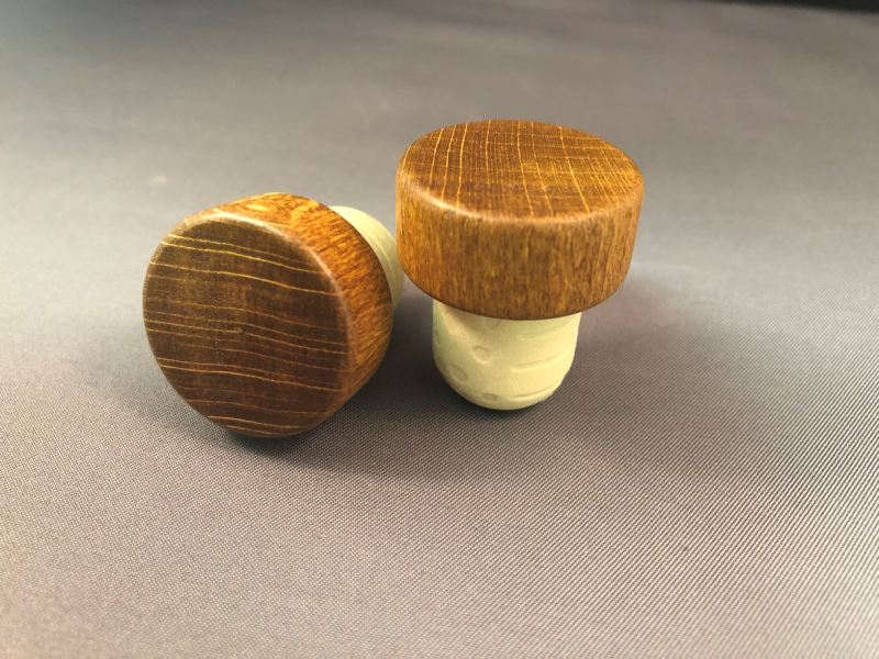Two wooden wine stoppers on a grey surface.