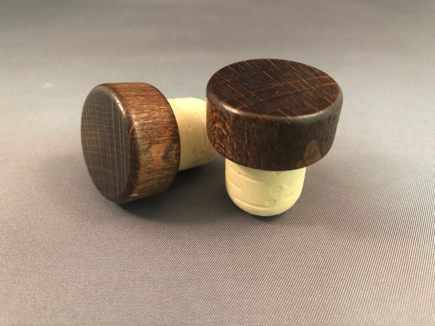 Two Walnut 29x13/19.5 wine stoppers on a grey surface.
